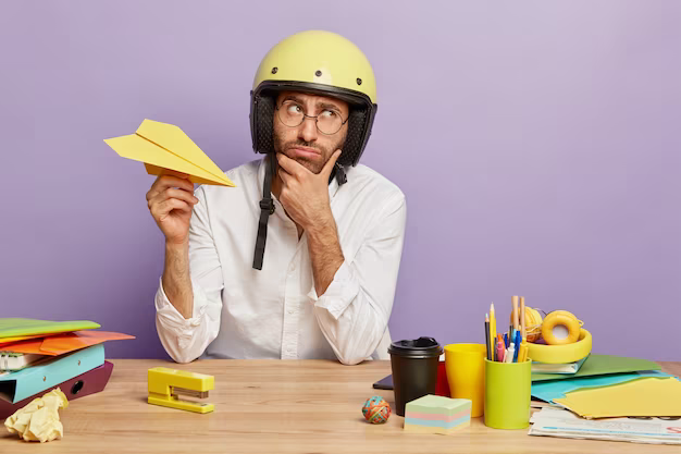 Thoughtful man, tired from work in the office, holding a paper airplane